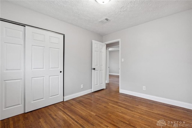 unfurnished bedroom with visible vents, baseboards, wood finished floors, a closet, and a textured ceiling