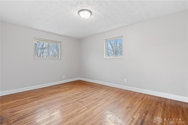 spare room featuring a healthy amount of sunlight, a textured ceiling, baseboards, and wood finished floors