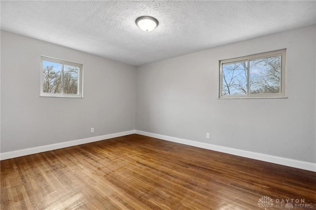 empty room with a textured ceiling, baseboards, and wood finished floors