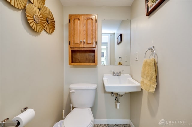 half bath with toilet, baseboards, and a sink