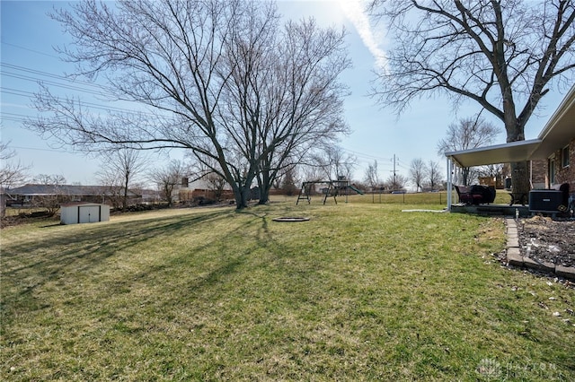 view of yard featuring a storage unit, central AC, fence, a playground, and an outdoor structure