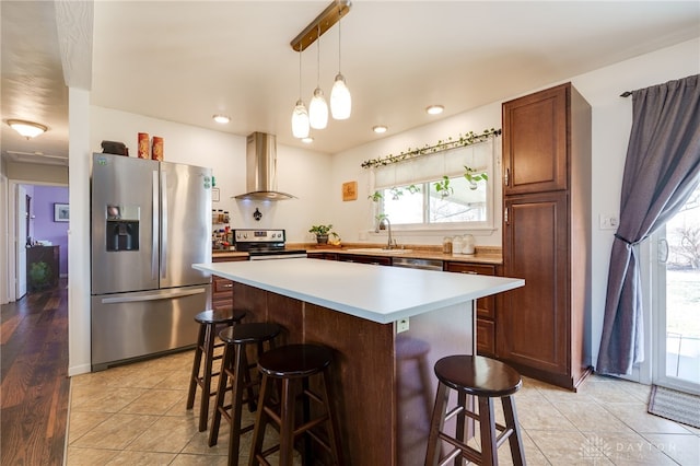 kitchen with a sink, a kitchen breakfast bar, a kitchen island, stainless steel appliances, and wall chimney range hood