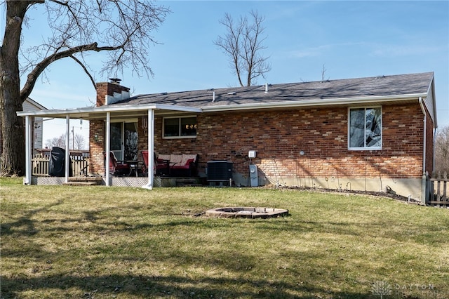 rear view of house featuring cooling unit, an outdoor fire pit, a chimney, a lawn, and brick siding