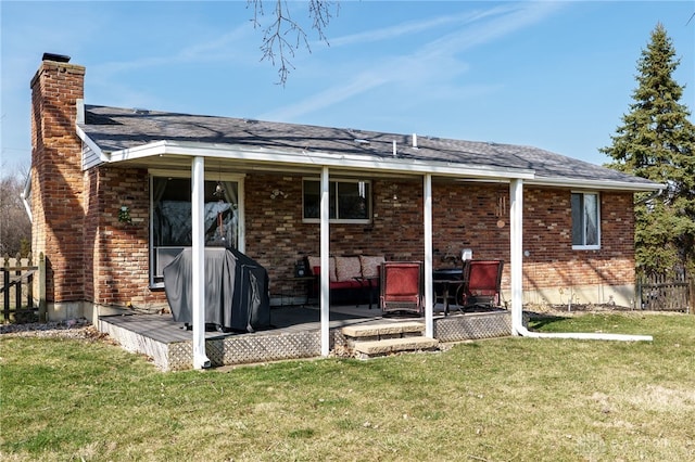 rear view of house with brick siding, a lawn, a chimney, and fence