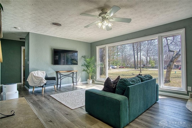 living area with baseboards, wood finished floors, visible vents, and a textured ceiling