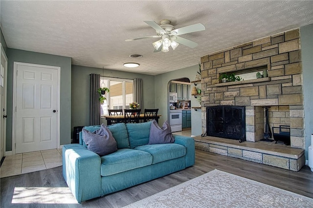 living room with wood finished floors, visible vents, arched walkways, ceiling fan, and a textured ceiling