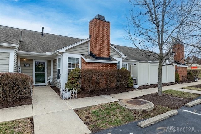 view of front of home featuring a shingled roof, fence, and a chimney