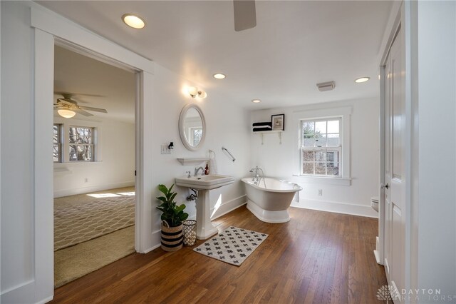 bathroom featuring a freestanding bath, wood finished floors, a ceiling fan, and toilet