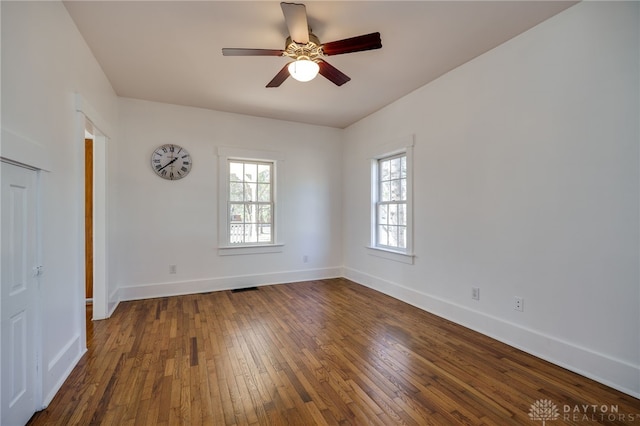 empty room featuring a ceiling fan, visible vents, dark wood-style floors, and baseboards