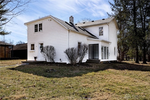 back of house featuring entry steps, a chimney, a yard, and roof with shingles