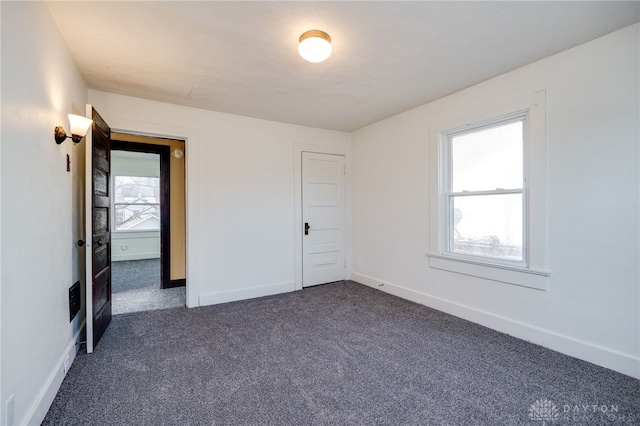 unfurnished room with baseboards and dark carpet