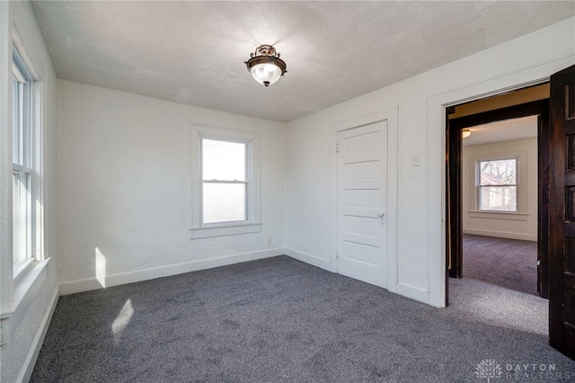 carpeted spare room featuring a textured wall, baseboards, and a textured ceiling