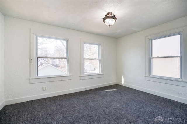 empty room with dark colored carpet, baseboards, and a textured wall