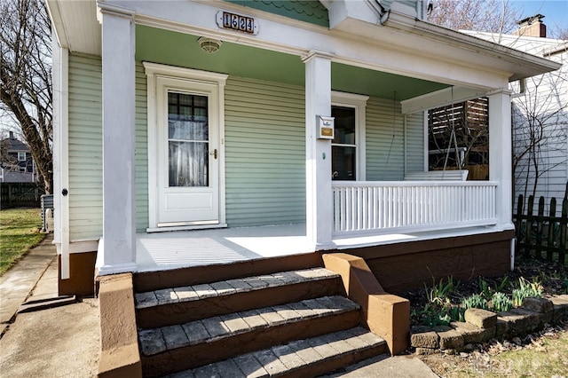 view of exterior entry with a porch and fence