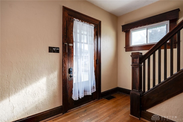 foyer entrance with visible vents, hardwood / wood-style flooring, stairway, baseboards, and a textured wall