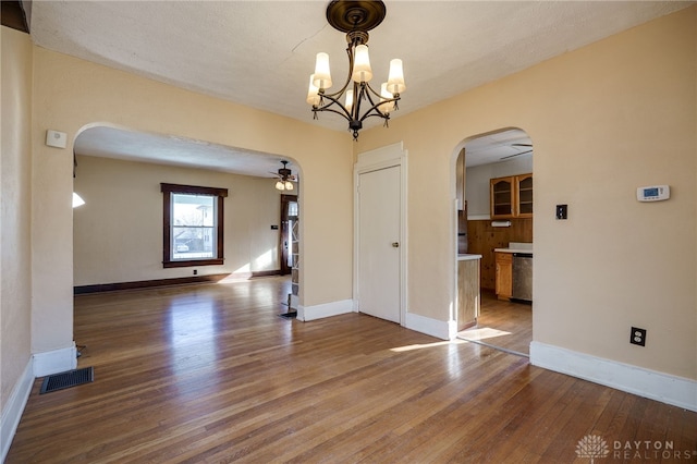 unfurnished room with visible vents, baseboards, arched walkways, hardwood / wood-style flooring, and ceiling fan with notable chandelier