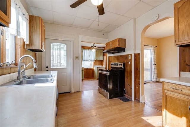 kitchen featuring light wood-type flooring, stainless steel range with electric stovetop, a sink, under cabinet range hood, and arched walkways