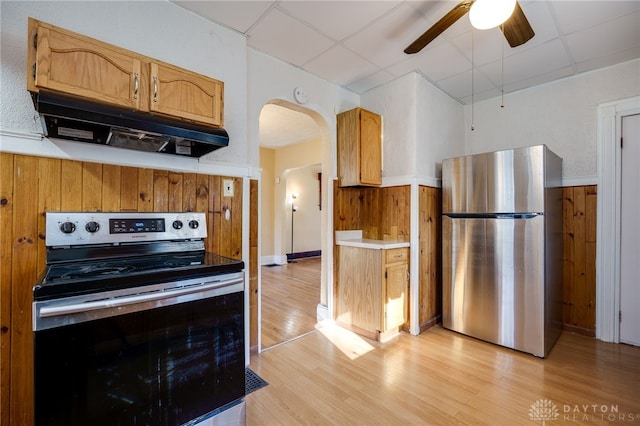 kitchen with arched walkways, a drop ceiling, light wood-style floors, under cabinet range hood, and appliances with stainless steel finishes