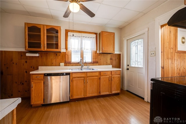 kitchen with brown cabinets, light wood-style flooring, a sink, stainless steel dishwasher, and light countertops