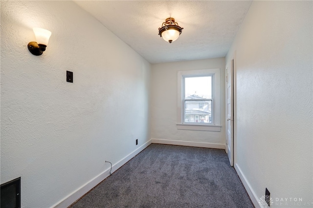 empty room with visible vents, baseboards, dark colored carpet, and a textured wall