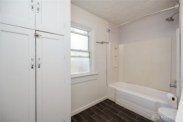 bathroom featuring baseboards, wood finish floors, tub / shower combination, a textured ceiling, and toilet