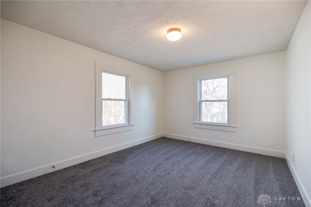 unfurnished room with a wealth of natural light, a textured ceiling, baseboards, and dark colored carpet