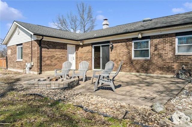 rear view of property with a fire pit, a shingled roof, brick siding, a chimney, and a patio area