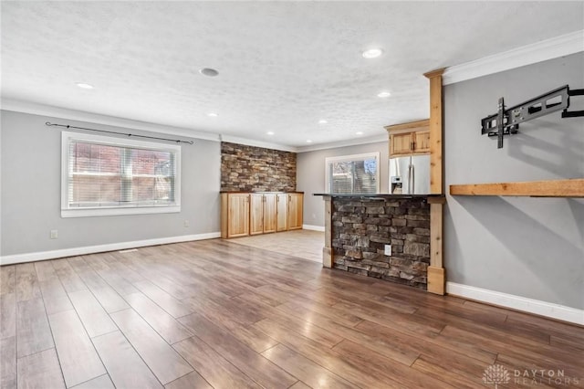 unfurnished living room featuring crown molding, wood finished floors, baseboards, and a healthy amount of sunlight