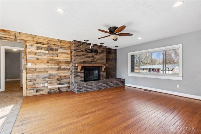 unfurnished living room featuring visible vents, baseboards, ceiling fan, a fireplace, and wood finished floors