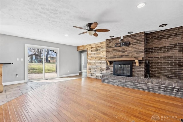 unfurnished living room with a brick fireplace, baseboards, ceiling fan, wood finished floors, and a textured ceiling