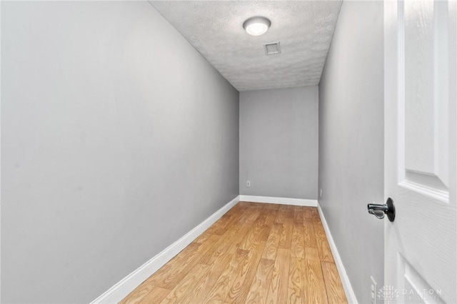 empty room featuring light wood-type flooring, baseboards, a textured ceiling, and visible vents