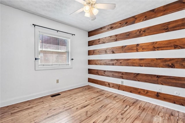 spare room with visible vents, wood-type flooring, baseboards, and a ceiling fan