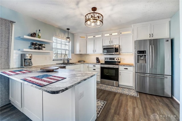 kitchen with appliances with stainless steel finishes, a peninsula, dark wood finished floors, and white cabinetry