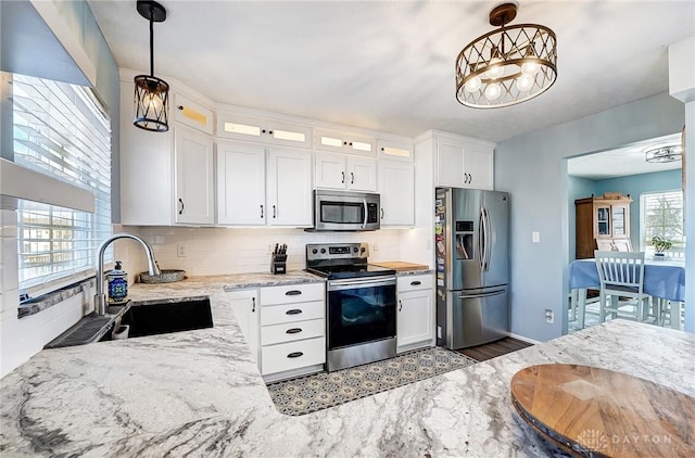 kitchen featuring a sink, light stone counters, tasteful backsplash, appliances with stainless steel finishes, and glass insert cabinets