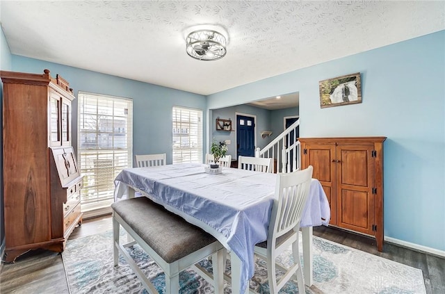 dining area with stairway, a textured ceiling, baseboards, and wood finished floors