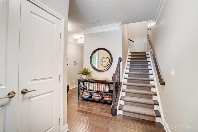 stairs with wood finished floors, baseboards, and ornamental molding