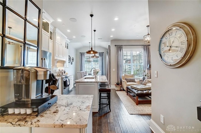 kitchen featuring a breakfast bar area, light stone counters, stainless steel range with gas cooktop, dark wood-style flooring, and a kitchen island with sink