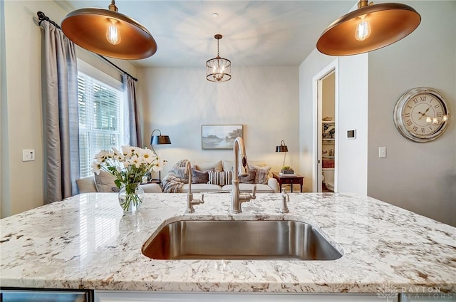 kitchen featuring hanging light fixtures, light stone counters, open floor plan, and a sink