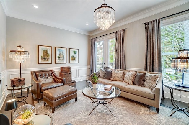 living room featuring a wainscoted wall, wood finished floors, an inviting chandelier, crown molding, and a decorative wall