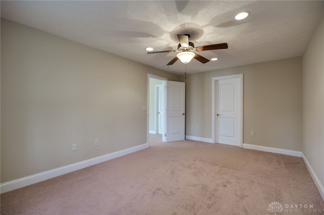 spare room with light carpet, a textured ceiling, a ceiling fan, and baseboards