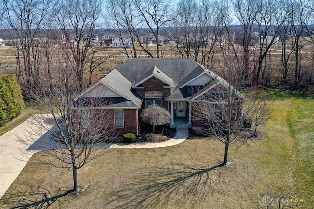 view of front of home with driveway, brick siding, a front yard, and a shingled roof