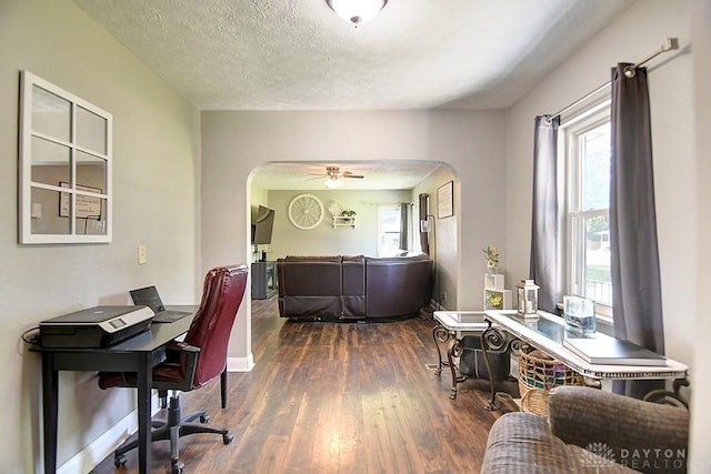 office space featuring arched walkways, a textured ceiling, baseboards, and wood finished floors