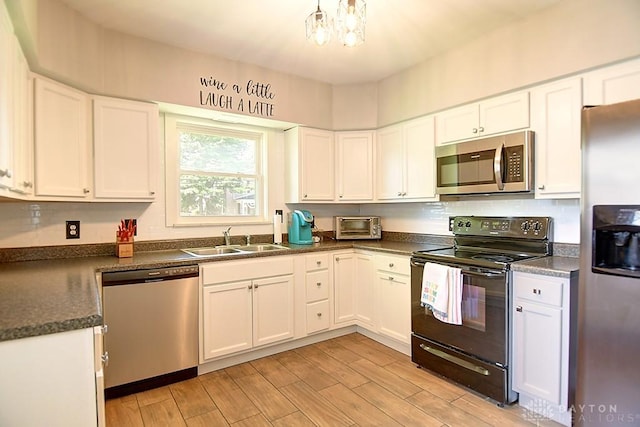 kitchen featuring a sink, white cabinets, appliances with stainless steel finishes, dark countertops, and light wood-type flooring