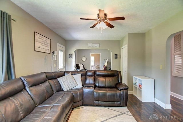 living area featuring a ceiling fan, baseboards, arched walkways, dark wood-style flooring, and a textured ceiling