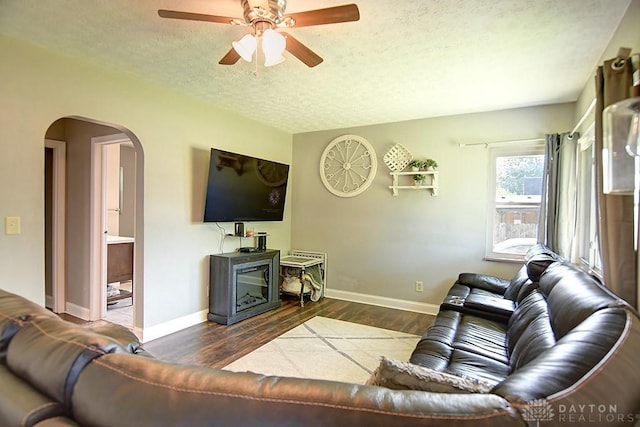 living room featuring a textured ceiling, wood finished floors, arched walkways, baseboards, and ceiling fan