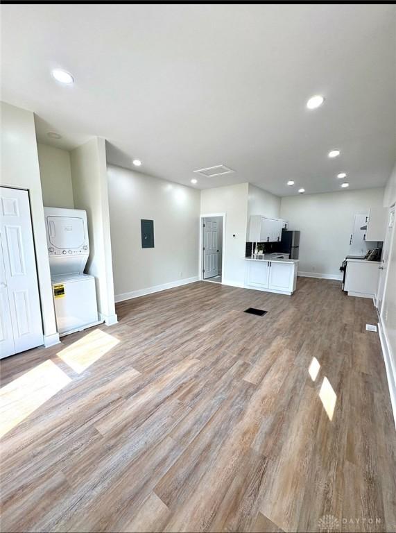 unfurnished living room with baseboards, electric panel, recessed lighting, light wood-style floors, and stacked washer / dryer