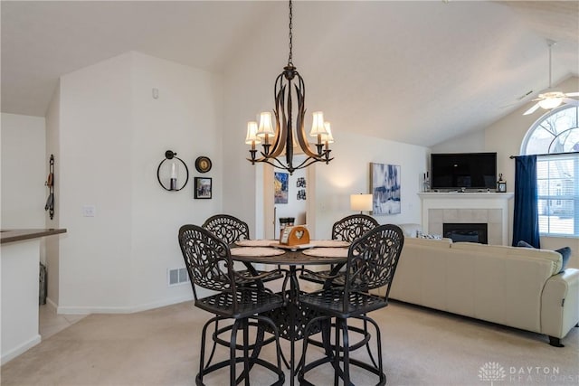 dining space featuring visible vents, lofted ceiling, light carpet, a tiled fireplace, and ceiling fan with notable chandelier