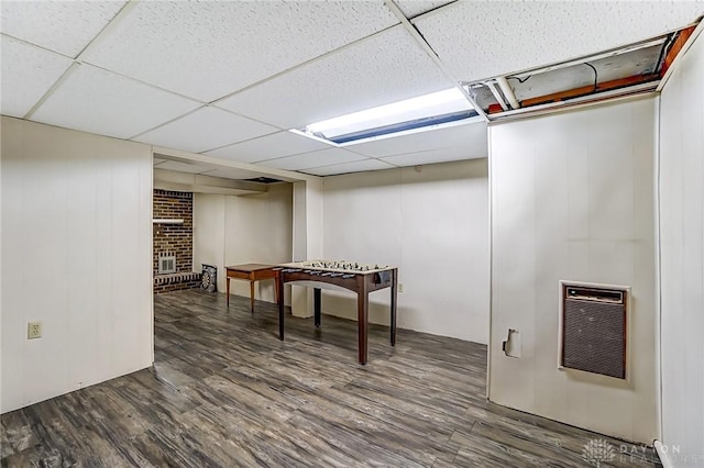 finished basement featuring a brick fireplace, heating unit, wood finished floors, and a drop ceiling