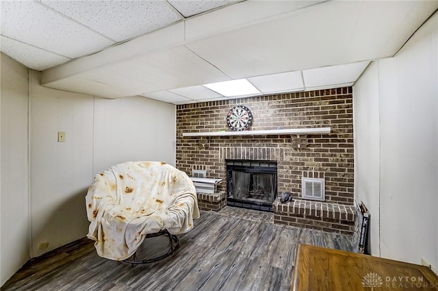 living area featuring wood finished floors, a fireplace, visible vents, and a paneled ceiling