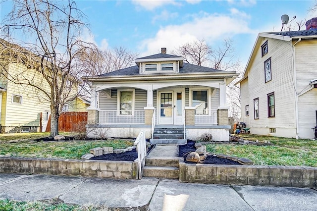 view of front facade featuring a porch, a chimney, and fence